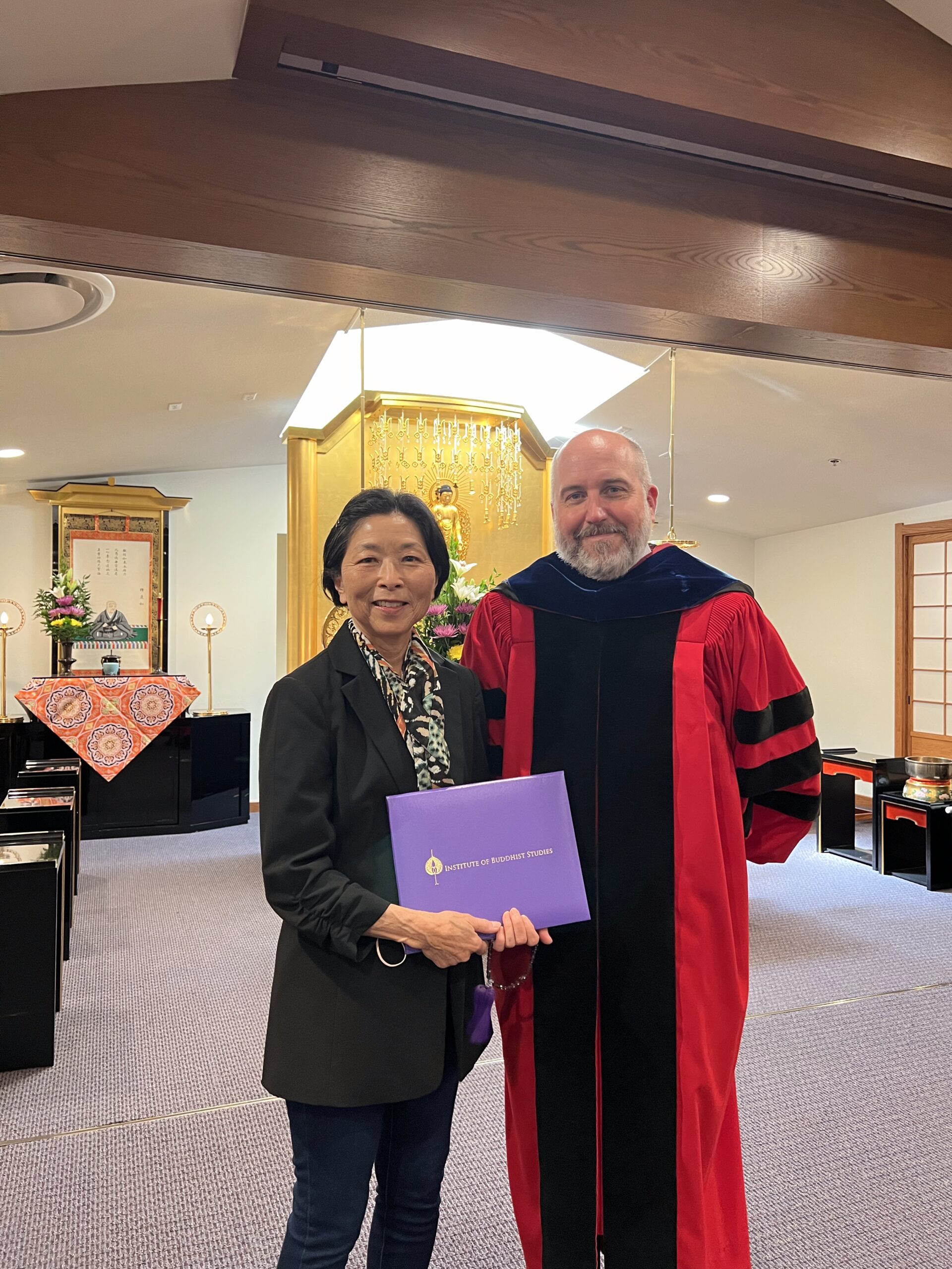 Two people smiling for camera, one holds a purple envelope