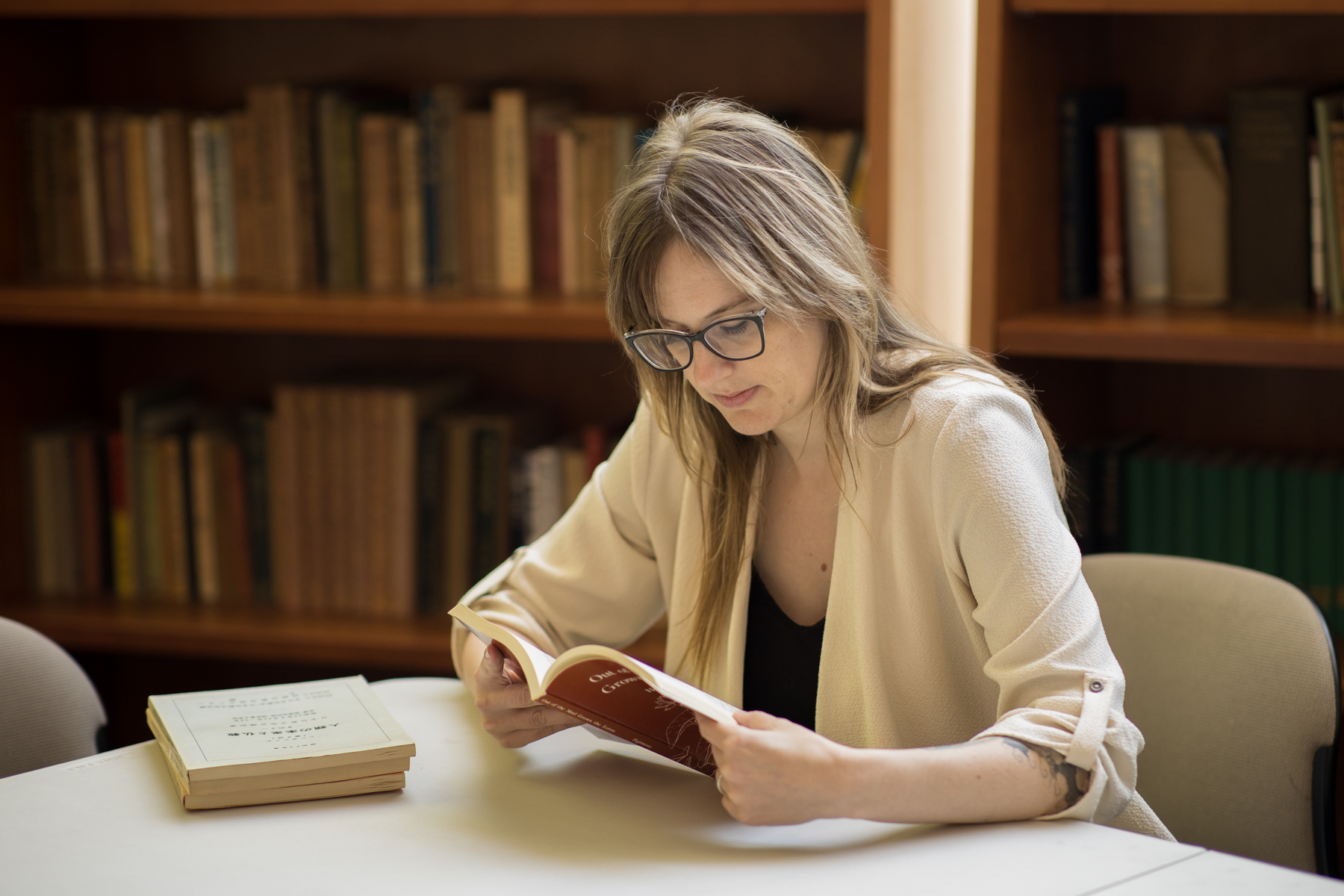 Blonde woman reading book in library setting